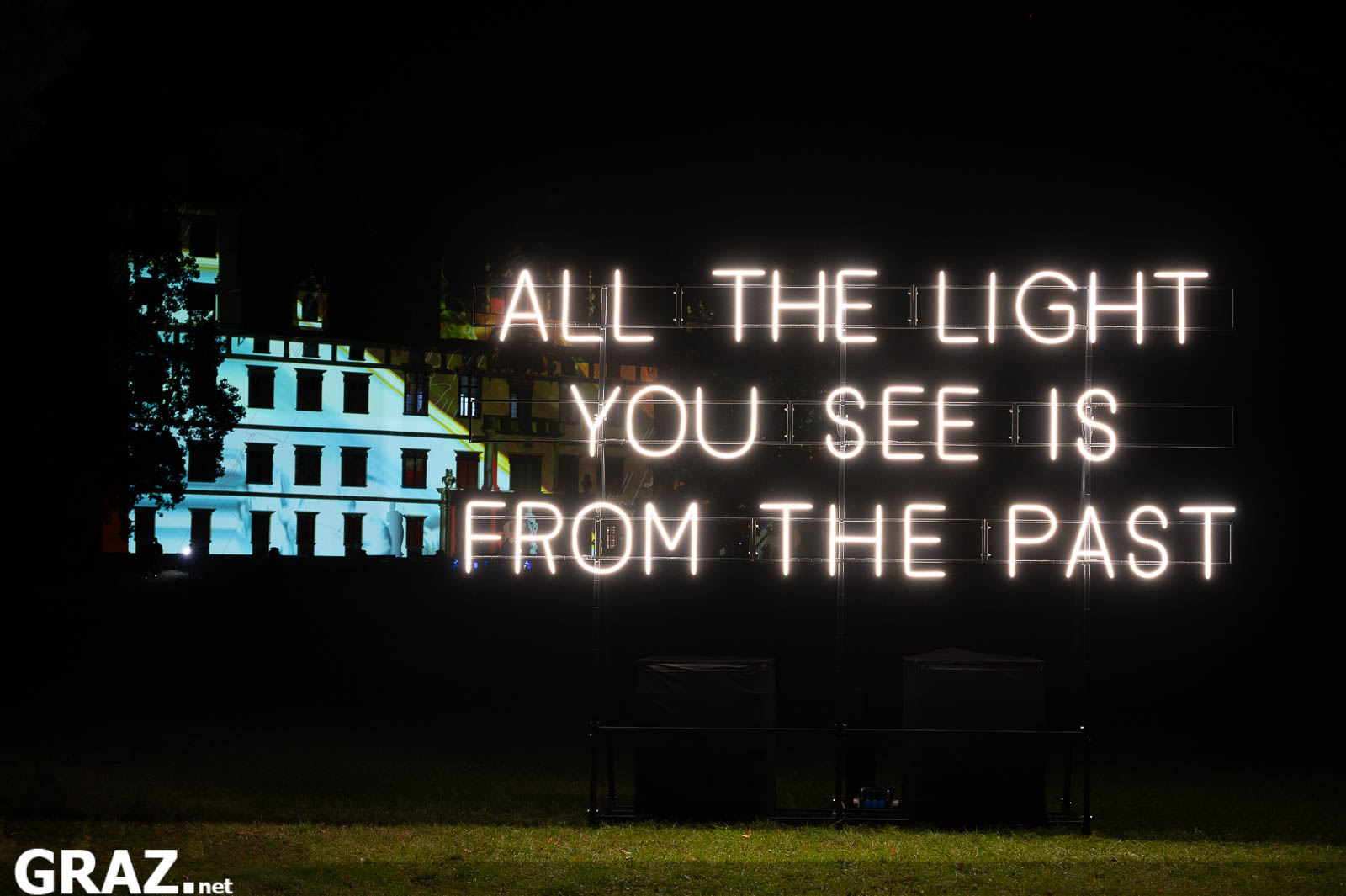 Alicia Eggerts leuchtende Schriftinstallation „All the light you see“ im Schlosspark, dahinter die beleuchtete Fassade von Schloss Eggenberg.