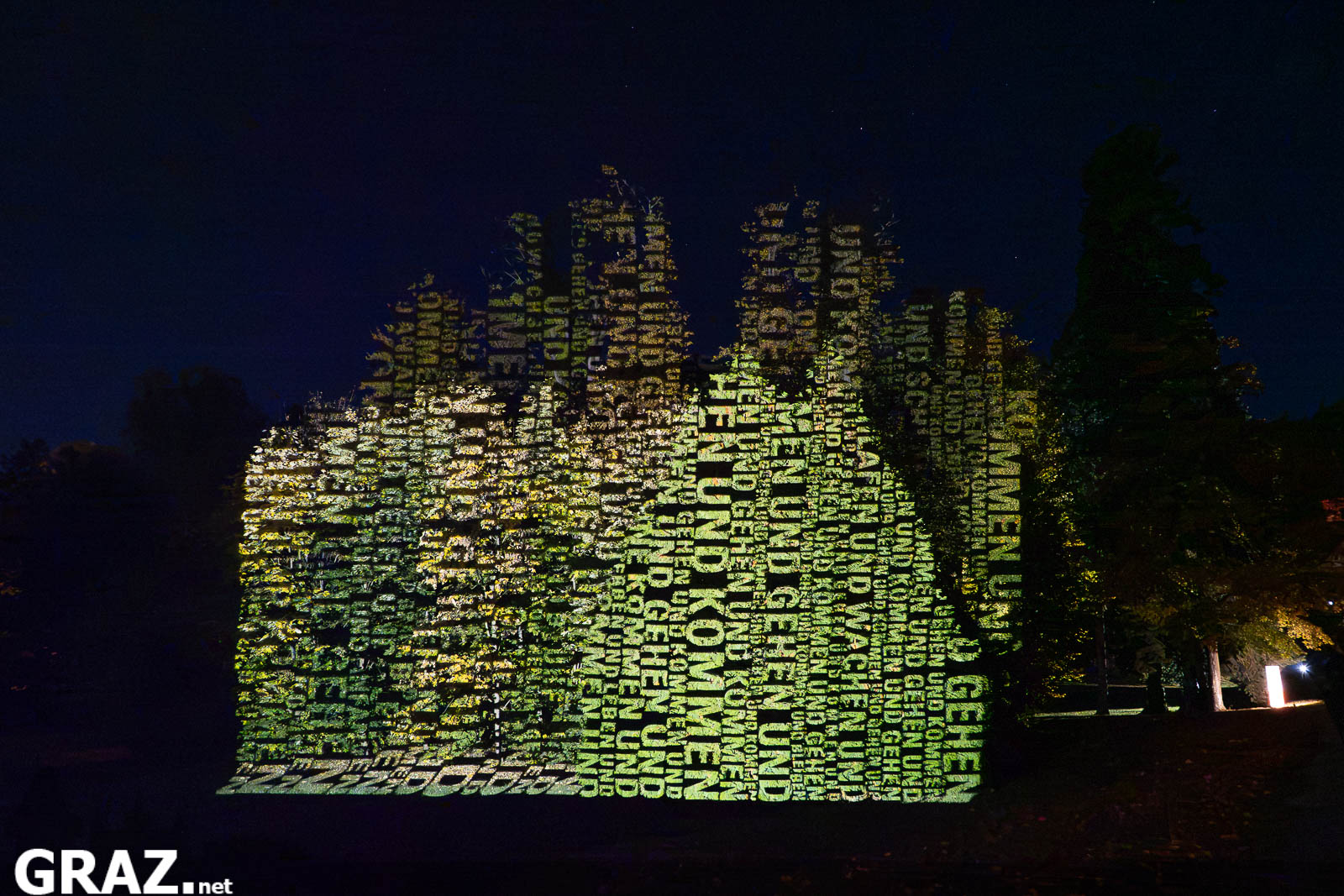 Leuchtende Wörter von „Räume der Zeit“ von Hartung & Trenz bedecken Baumkronen im Schlosspark Eggenberg bei Klanglicht 2026.