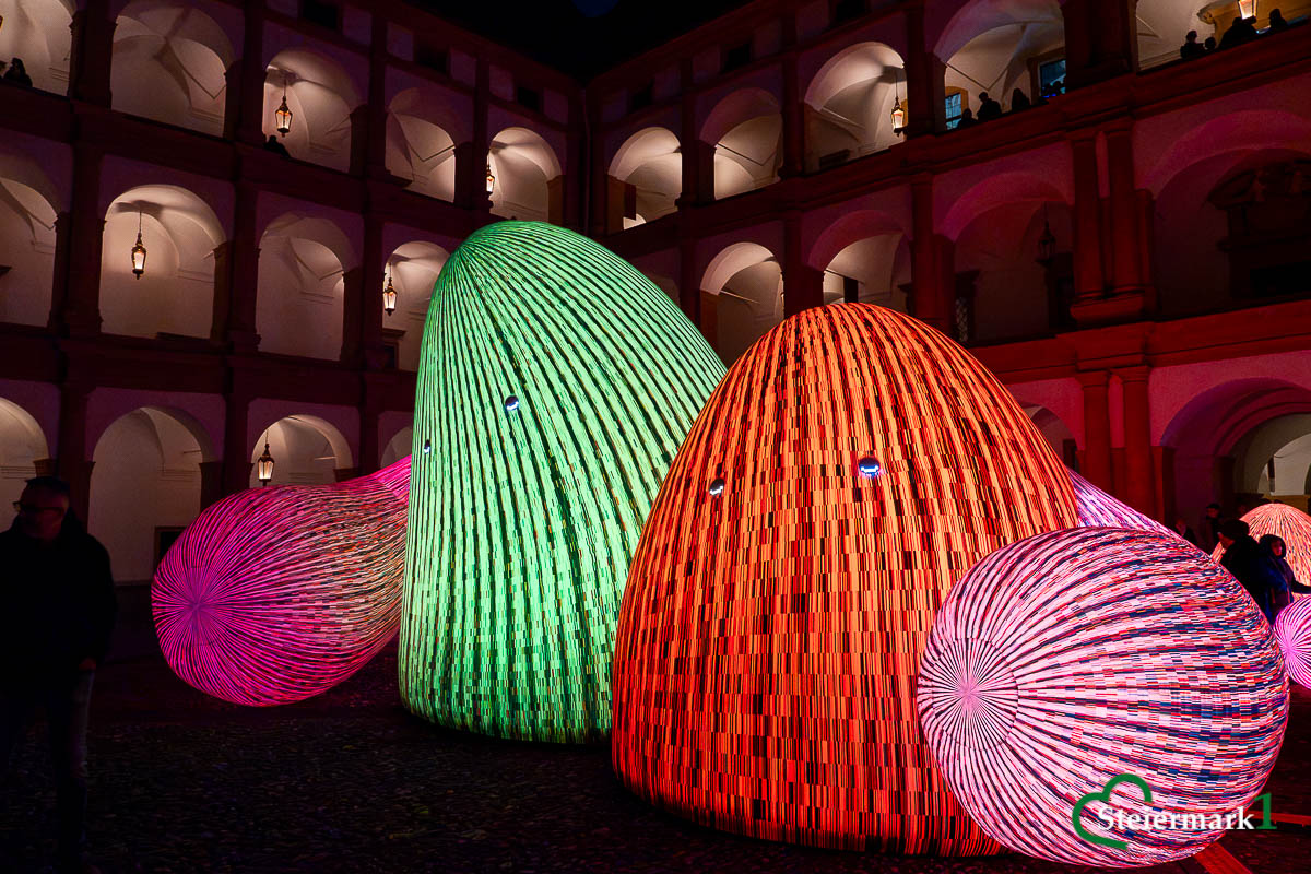 Grün und orange leuchtende Bergfiguren aus „Whispering Mountains“ von ENESS im Schlosshof Eggenberg.