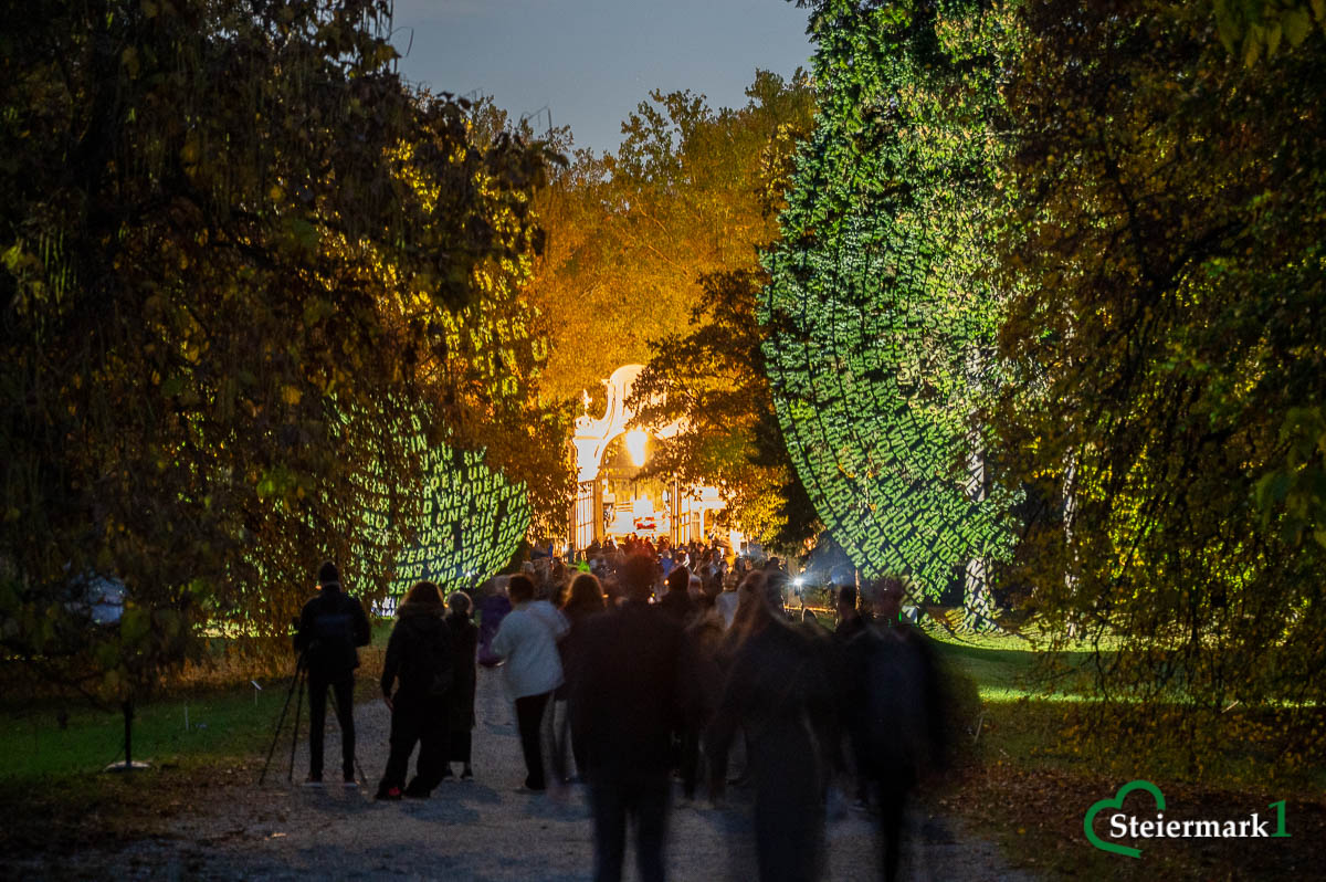 Gäste gehen durch die mit Textprojektionen von „Räume der Zeit“ von Hartung & Trenz beleuchtete Allee zum Schloss Eggenberg.