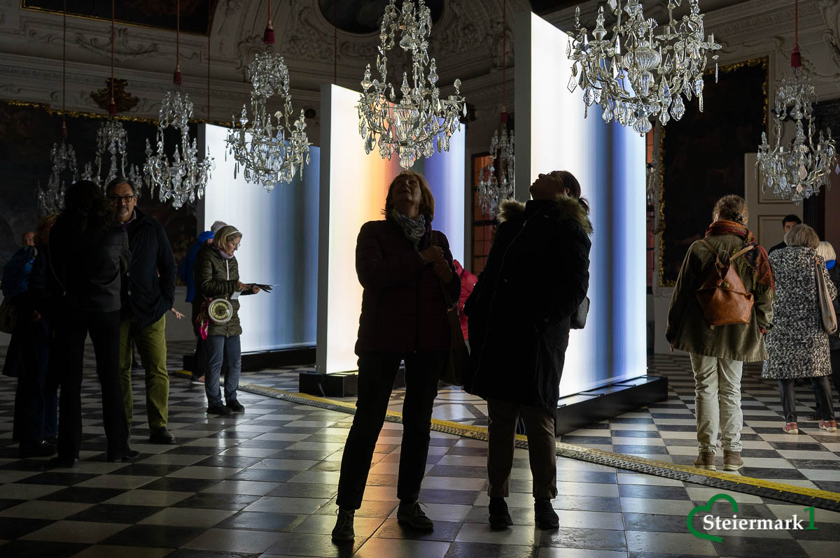 Gäste betrachten Inge Dicks „jahres licht weiss“ zwischen den Kronleuchtern des Planetensaals in Schloss Eggenberg.